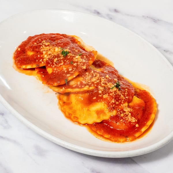 Ravioli with red sauce, grated cheese, and herbs on a white oval plate.