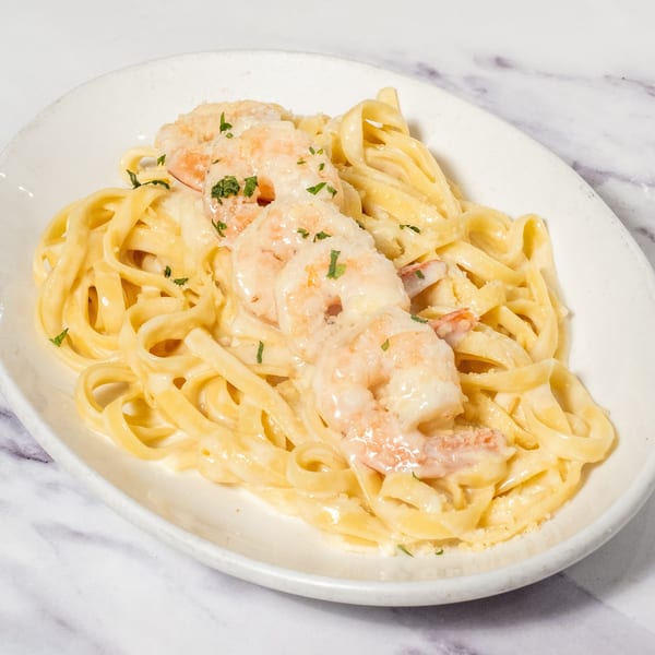 Creamy fettuccine pasta with shrimp and parsley on a white plate, from Ristorante da Maria.