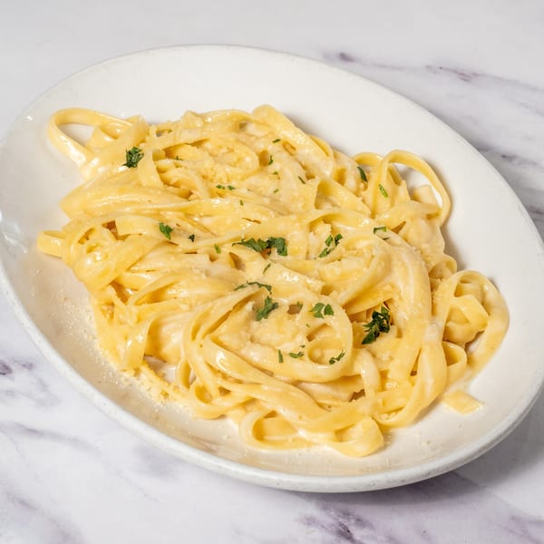 Creamy fettuccine alfredo pasta, garnished with fresh parsley and grated cheese, on a white oval plate.