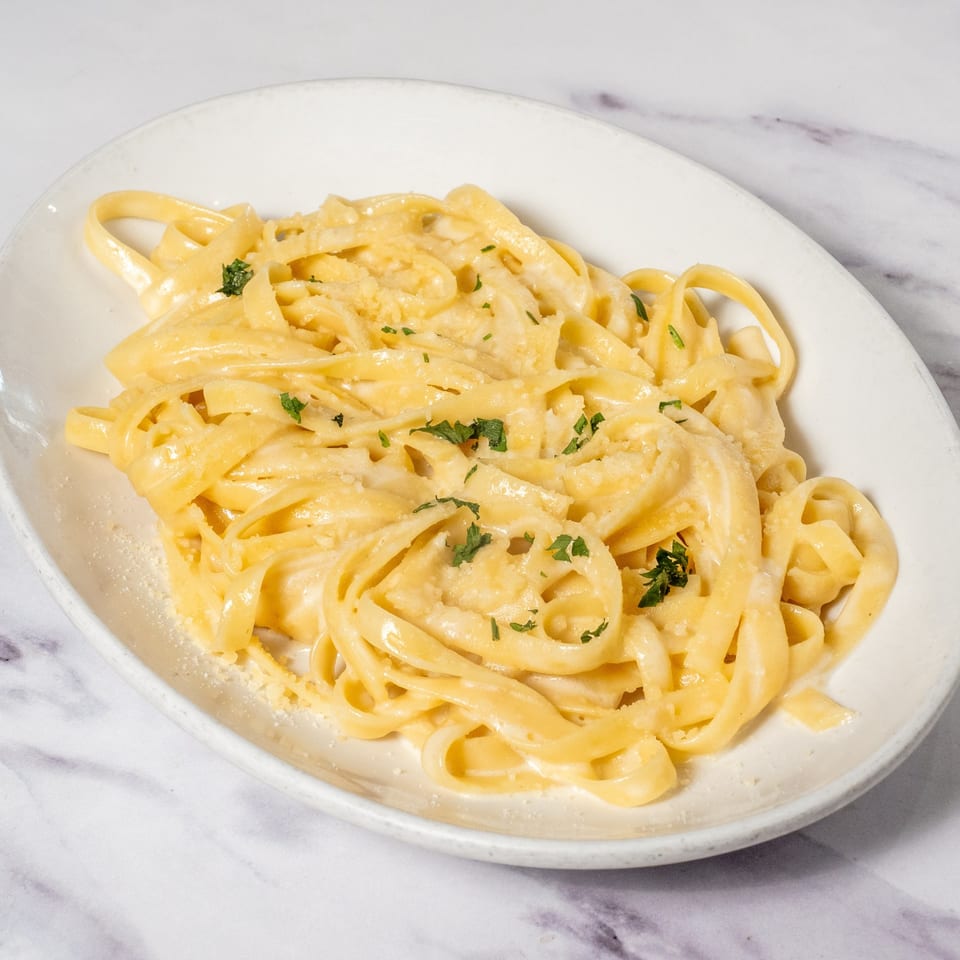 Creamy fettuccine alfredo pasta, garnished with fresh parsley and grated cheese, on a white oval plate.