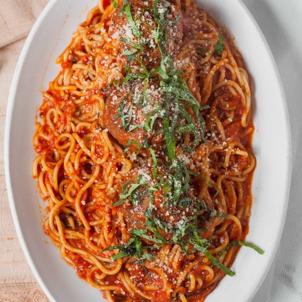 Spaghetti and meatballs with tomato sauce, parmesan cheese, and fresh basil on a white platter.